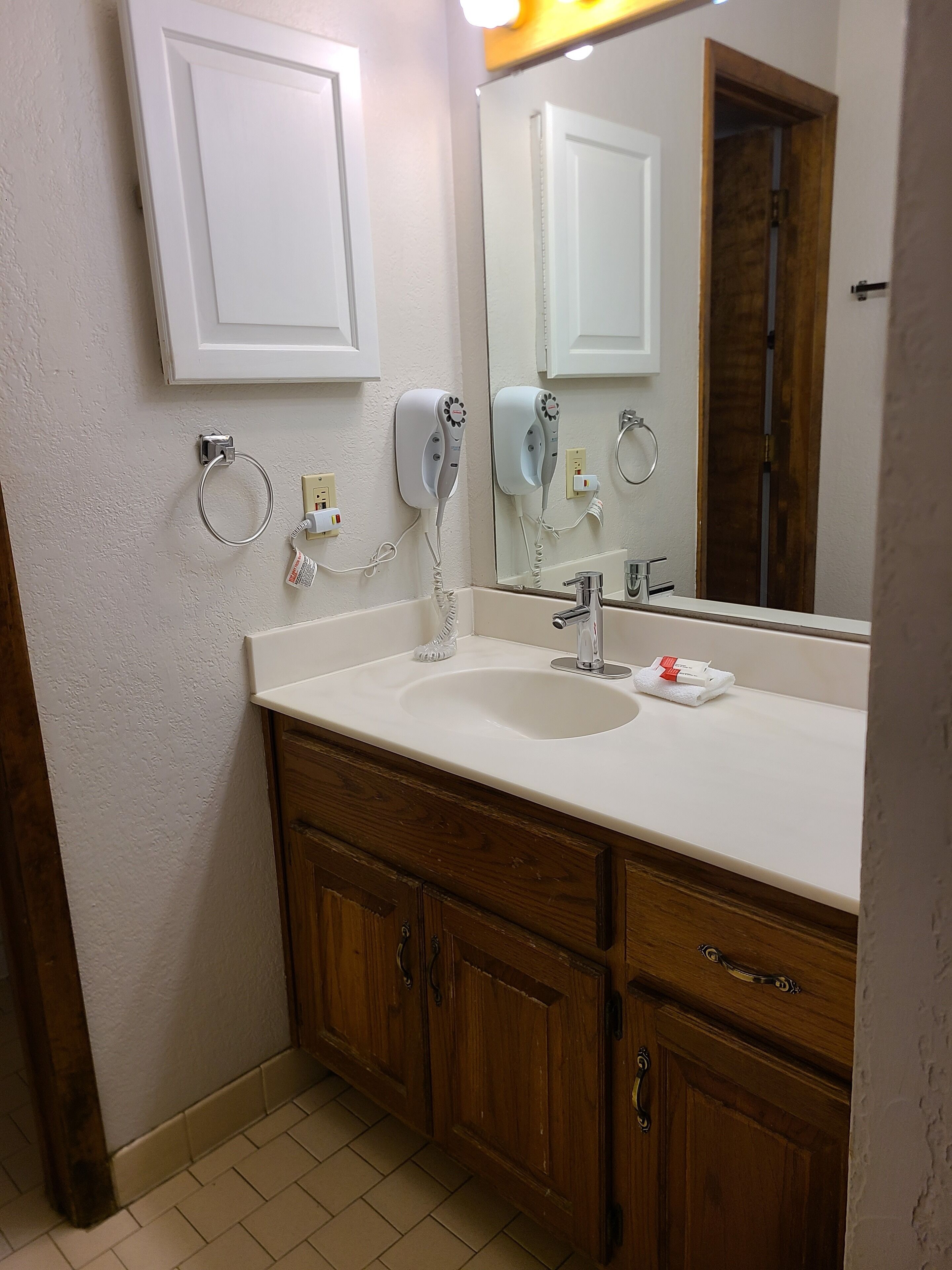 A bathroom with a white sink, wooden cabinets, a mirror, and two hair dryers mounted on the wall.