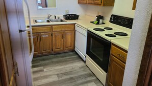 A compact kitchen with wooden cabinets, a white refrigerator, a stove, and a sink. - La Quinta Inn by Wyndham Farmington (Farmington)