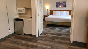 A hotel room with a bed, a small kitchenette, a microwave, and a nightstand with a lamp. - La Quinta Inn by Wyndham Farmington (Farmington)