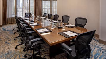 Una sala conferenze con un lungo tavolo, diverse sedie e un pavimento con tappeto.