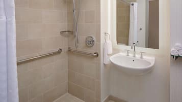 A modern bathroom with beige tiles, a walk-in shower, a sink with a mirror, and a towel rack.