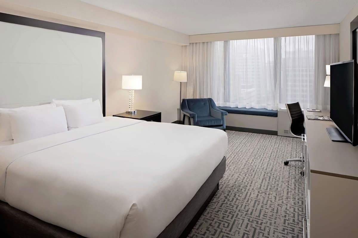 A hotel room with a large bed, a desk with a computer, a chair, and a TV.