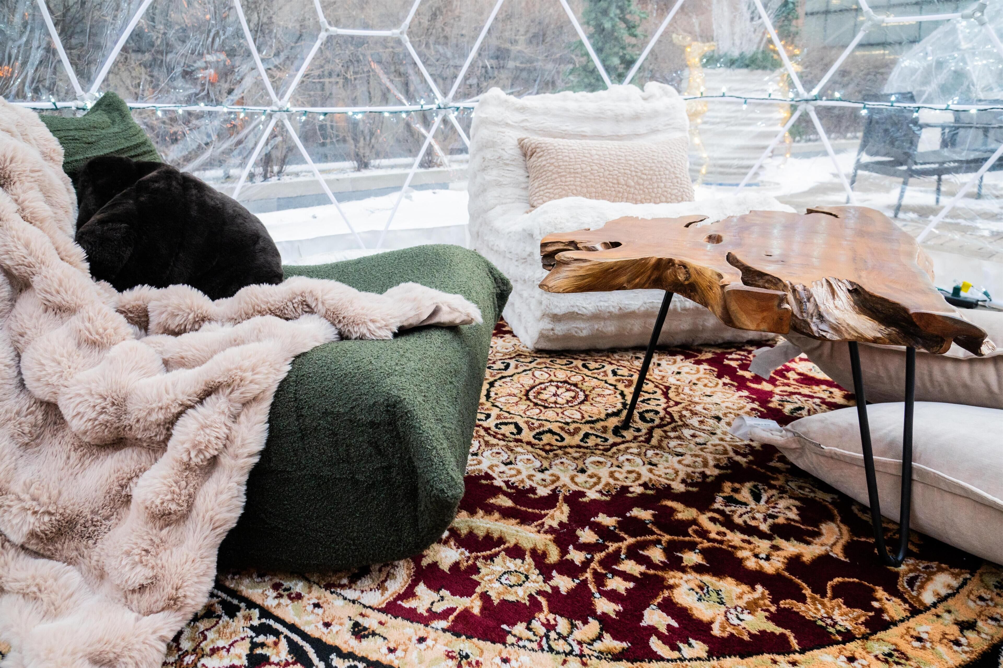 A cozy room with a green armchair, a white sofa, a patterned rug, and a wooden coffee table.
