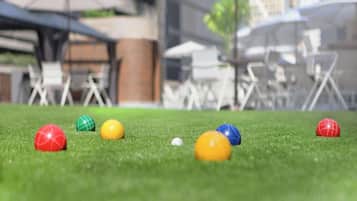 Une vue rapprochée d’un terrain de croquet, avec des balles colorées et un arrière-plan flou représentant des sièges installés à l’extérieur.