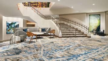Un vestíbulo moderno con una alfombra de diseño de mármol, una escalera con barandilla metálica y una zona de estar con una mesa redonda y sillas.