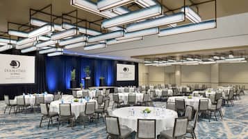 A conference room with round tables, chairs, and a stage with a presentation screen.