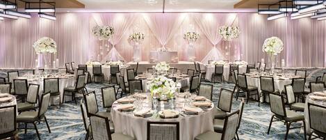A banquet hall with round tables, chairs, and floral centerpieces.