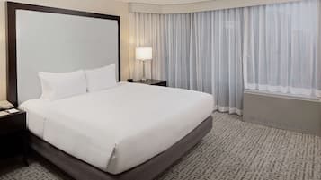 Una habitación de hotel con una cama grande, una mesita de noche con lámpara, una ventana con cortinas y un radiador.