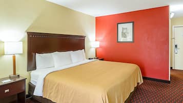 Habitación de hotel con una cama grande, una mesita de noche con lámpara, pared de acento roja y un cuadro enmarcado en la pared.
