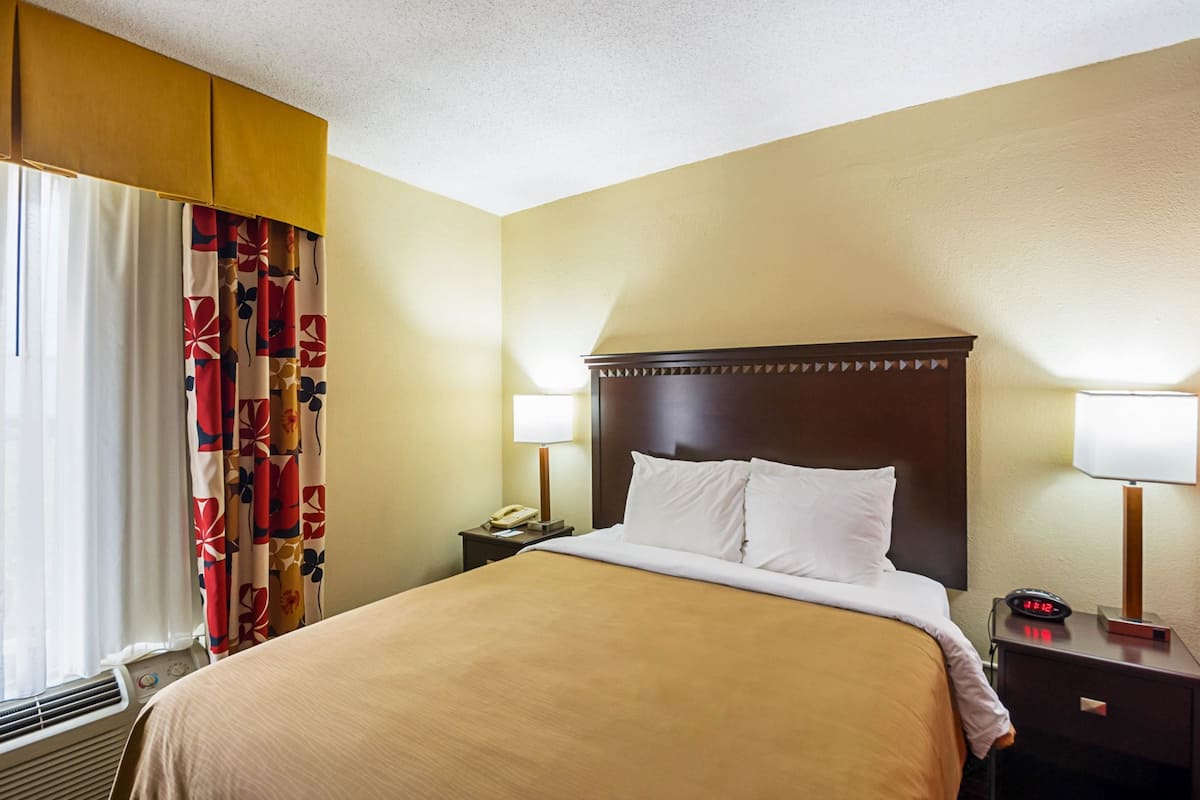 A hotel room with a large bed, two bedside tables with lamps, a telephone, and a window with curtains.
