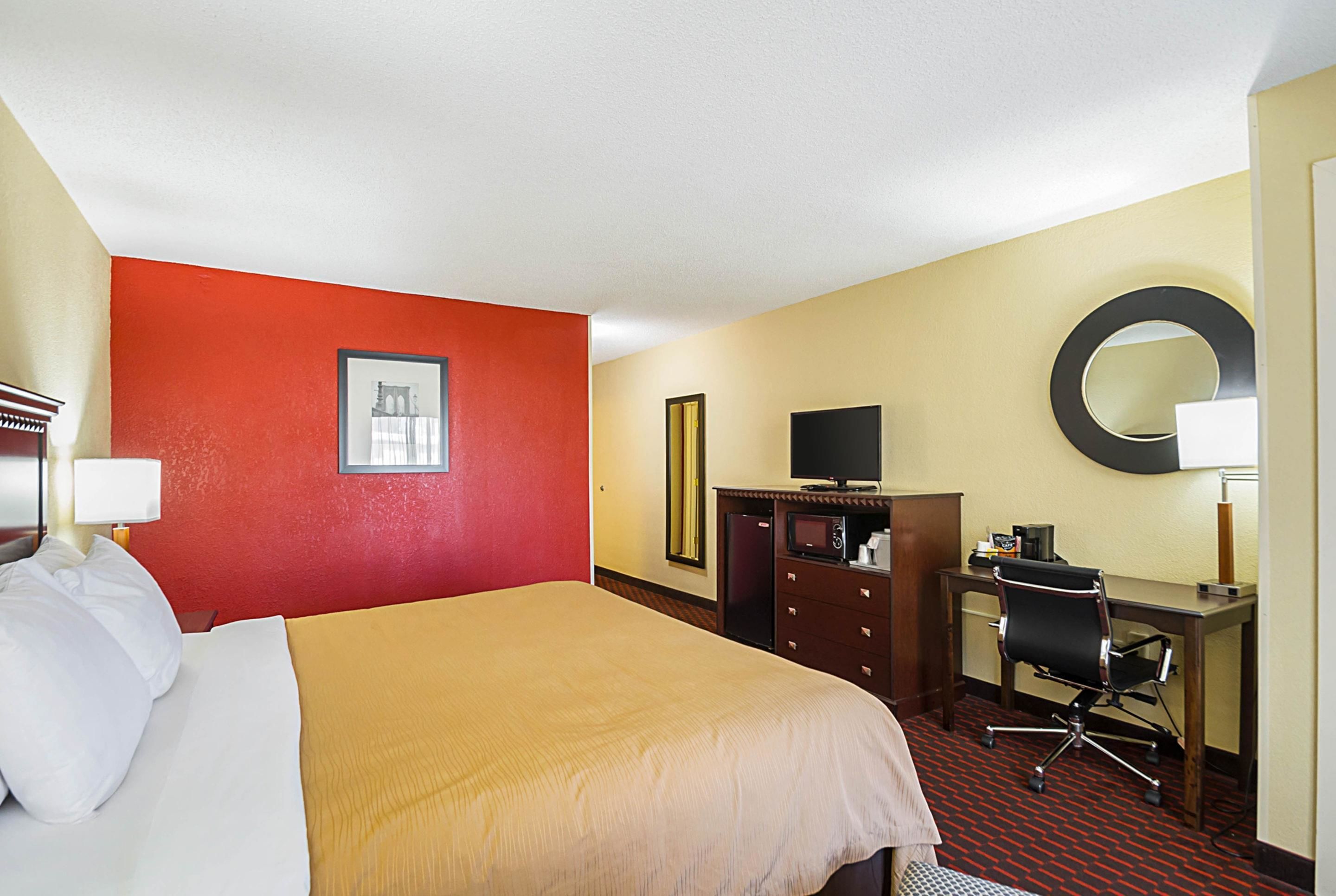 A hotel room with a bed, a desk, a chair, a television, a mirror, and a picture on the wall.