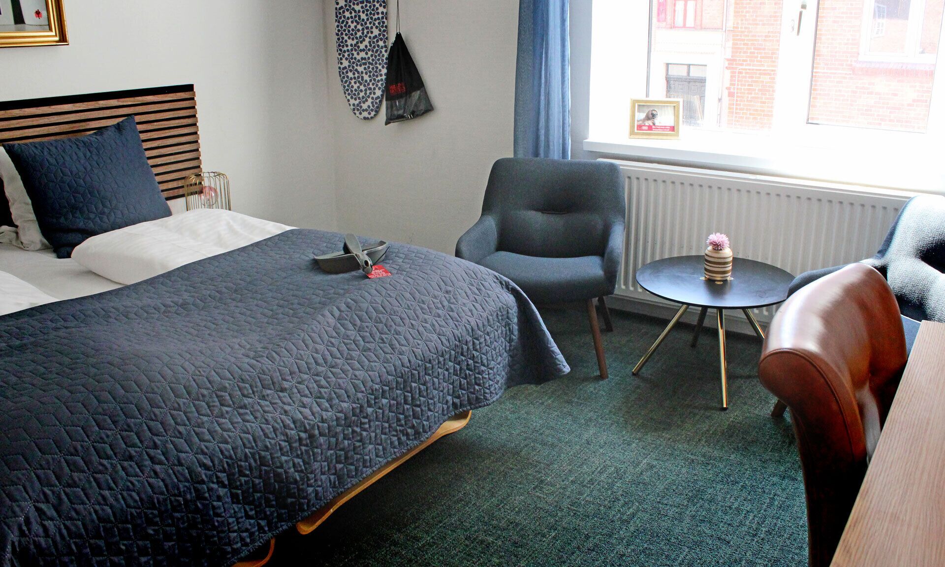 A hotel room with a bed, a chair, a small table, and a window with a view of buildings.
