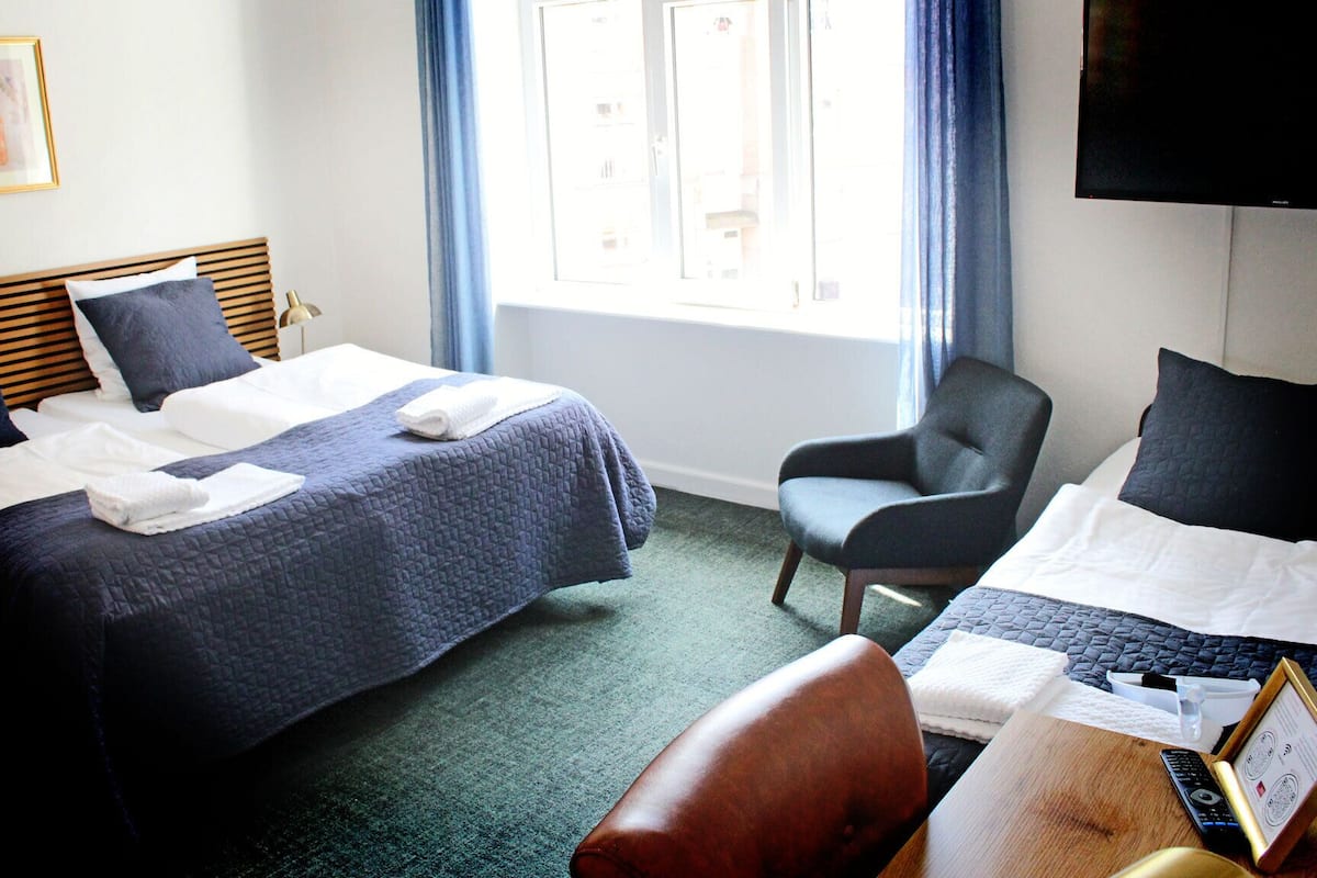 A hotel room with two beds, a chair, a desk with a computer, and a TV.
