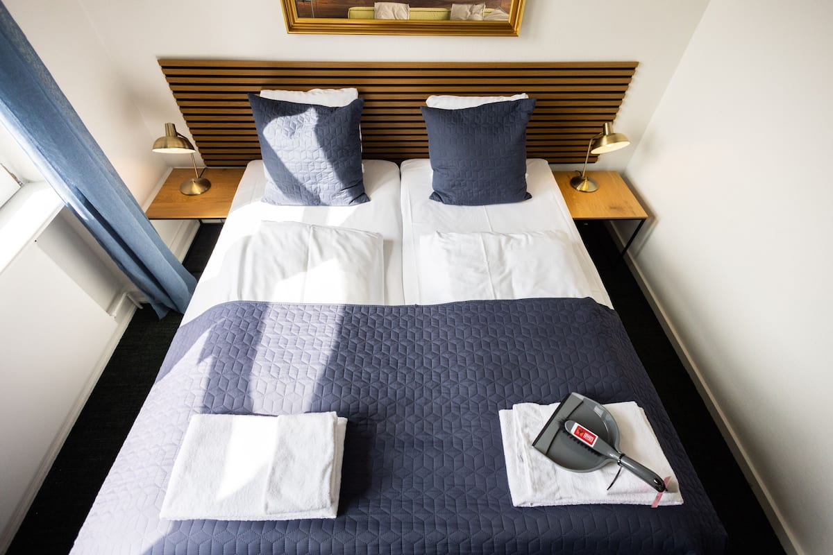 A neatly made bed with two pillows, a blue quilt, and a hairdryer on a towel.