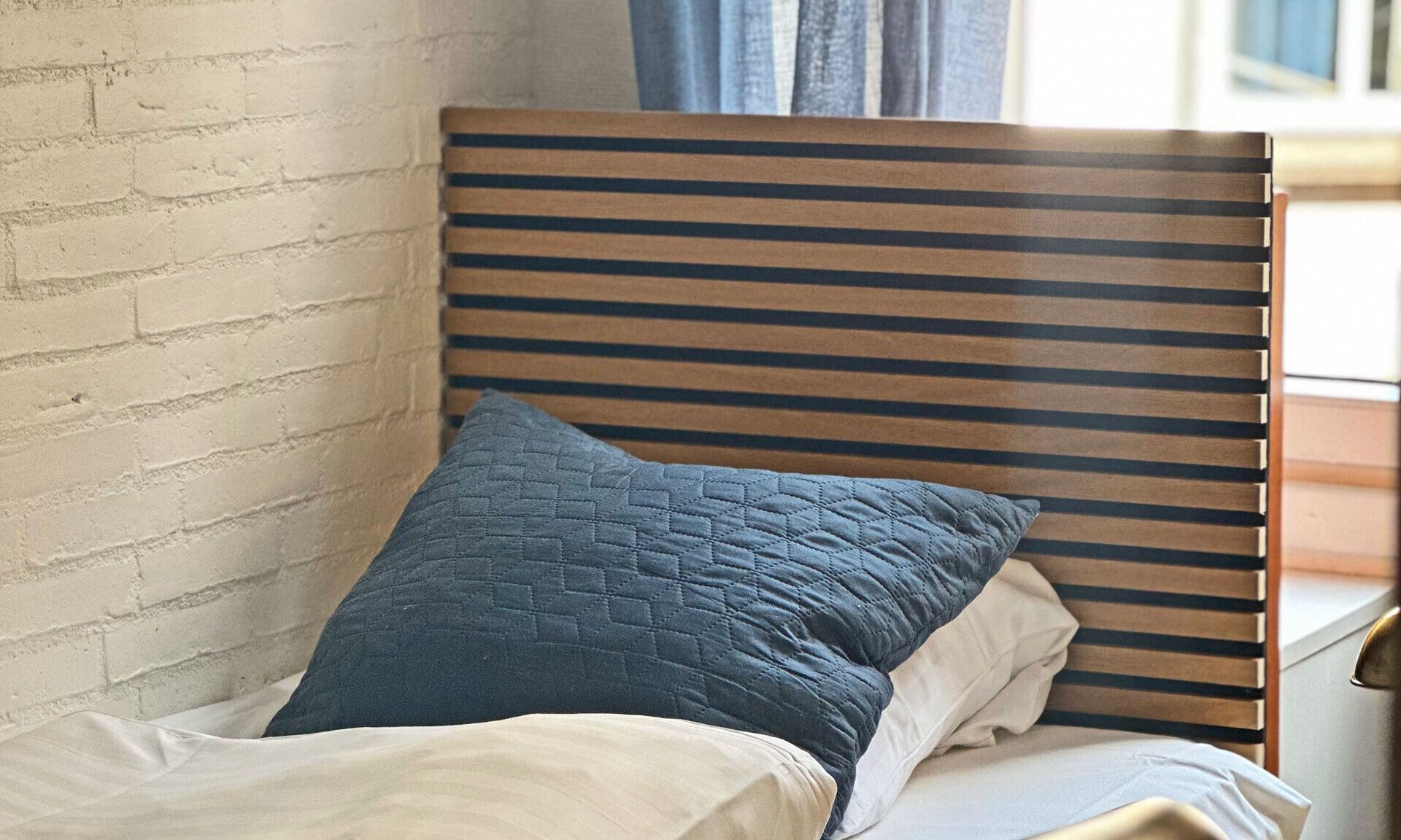 A bed with a wooden headboard, a blue quilted pillow, and white bedding.