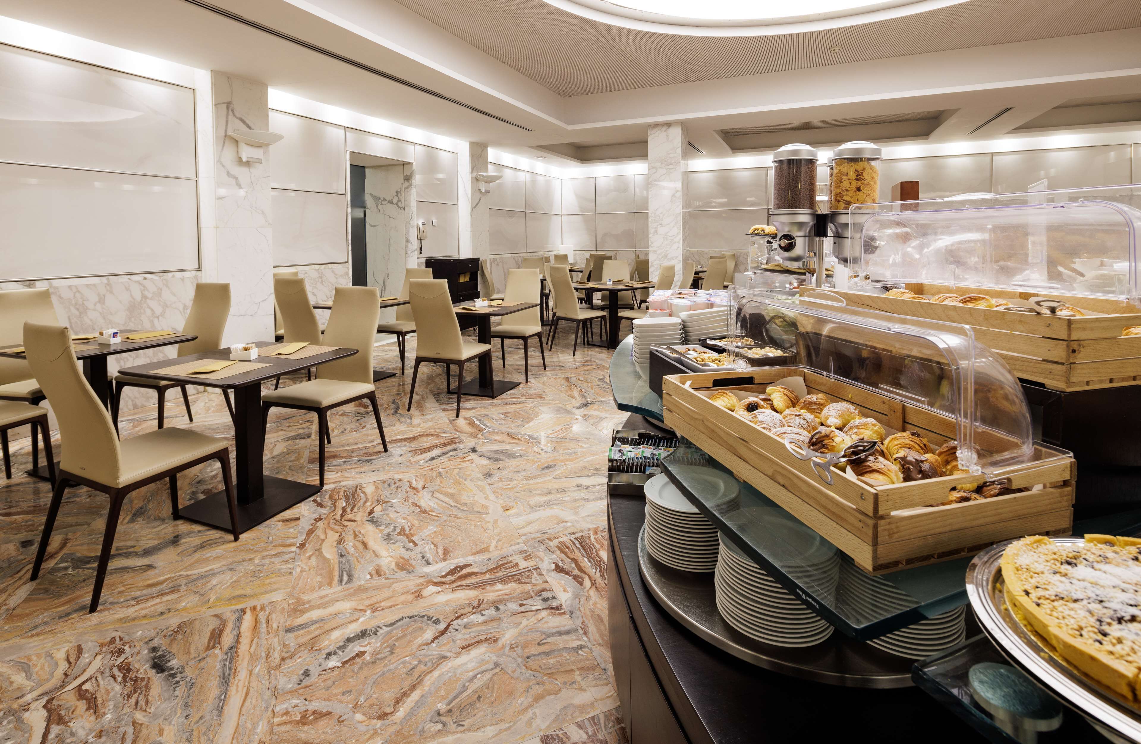 A hotel dining area with marble flooring, multiple tables with chairs, and a buffet with various food items.