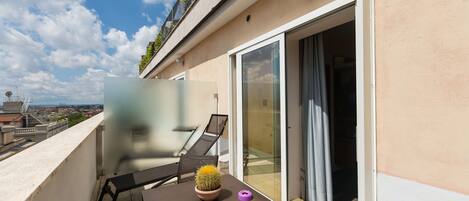 A balcony with a table, chairs, a potted cactus, and a sliding glass door.