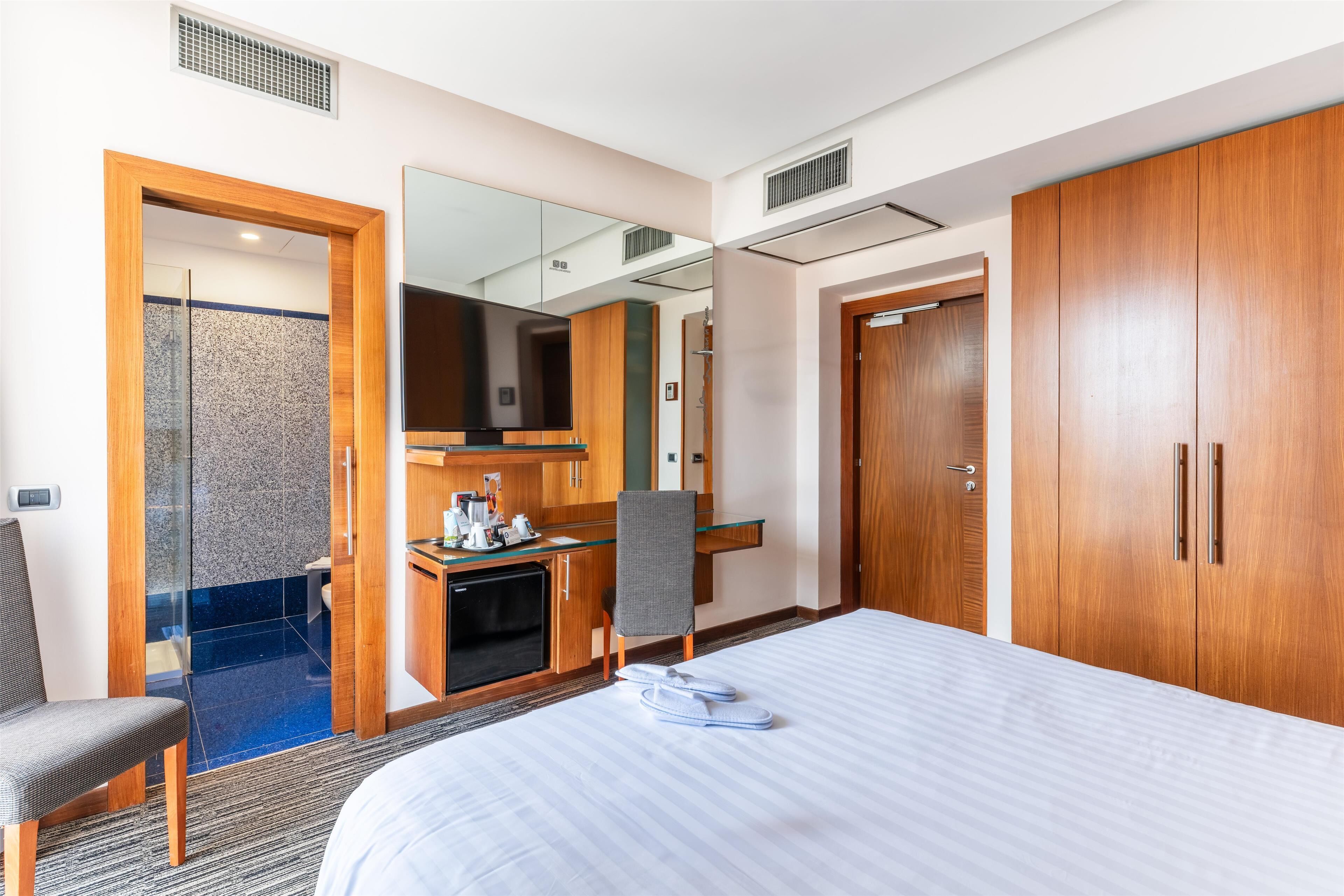 Une chambre d’hôtel comprenant un lit, un bureau avec un ordinateur, une chaise, une armoire et un espace douche.