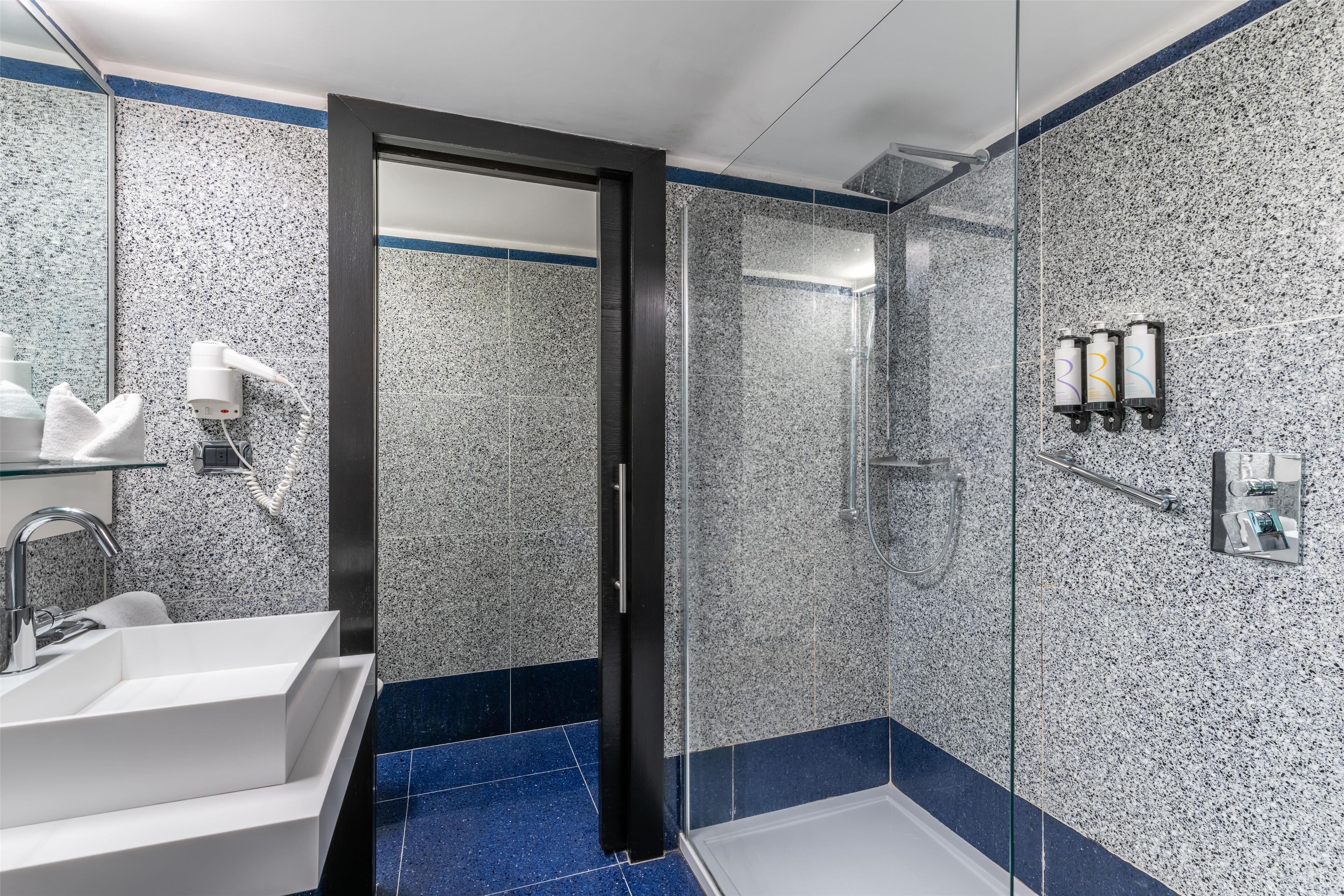 Un baño moderno con un lavamanos blanco, una cabina de ducha con mampara de vidrio y un suelo de azulejos azules.