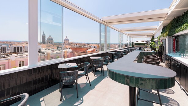 Un bar situé sur le toit, offrant une vue panoramique sur la ville, avec un comptoir incurvé et un espace salon.