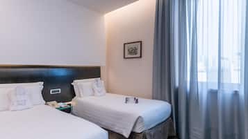 A hotel room with two beds, a headboard, a bedside table, a phone, a framed picture on the wall, and a window with curtains.