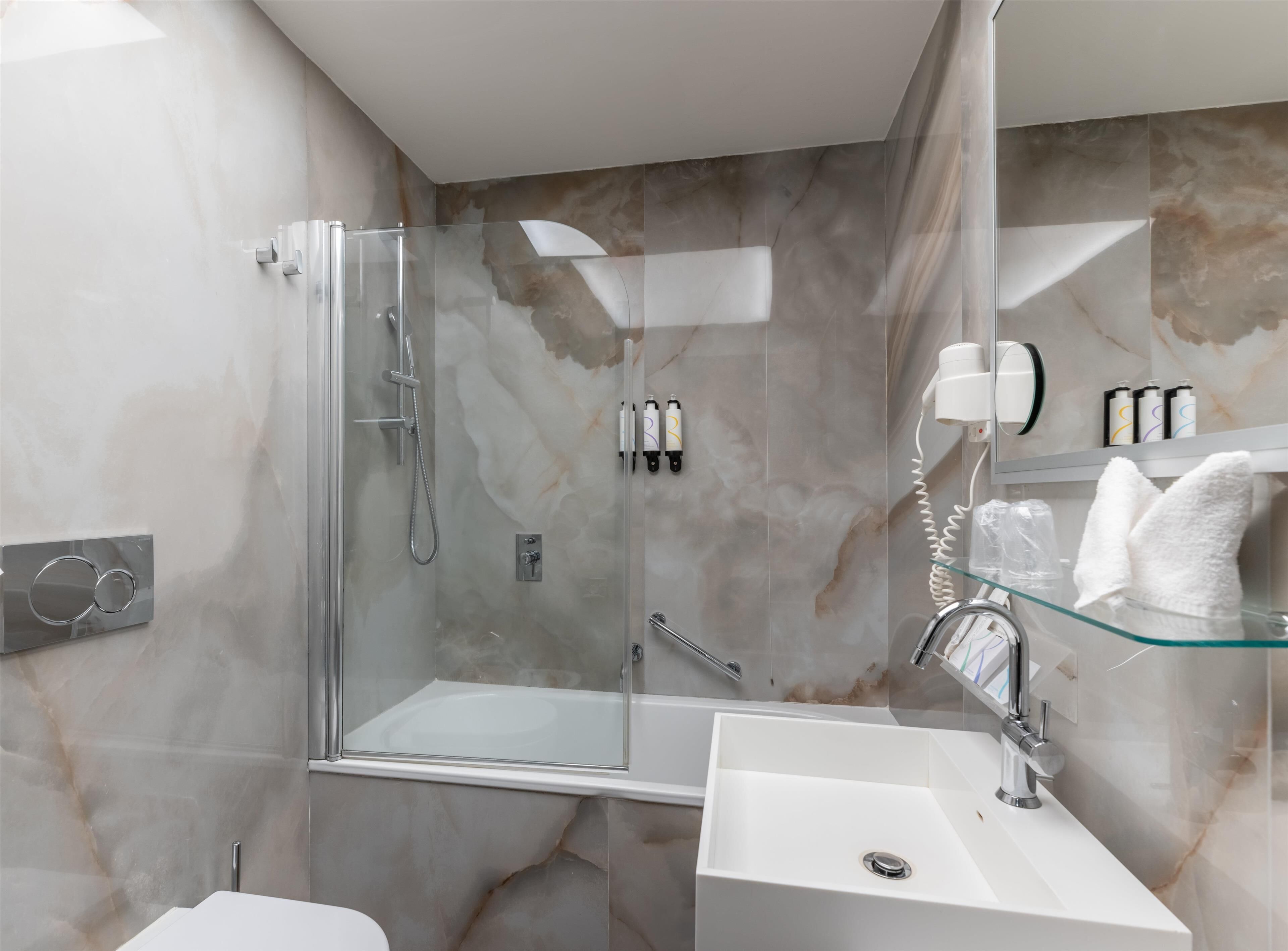 Une salle de bain moderne avec une douche à parois de verre, un lavabo blanc et une étagère en verre où sont rangés les articles de toilette.