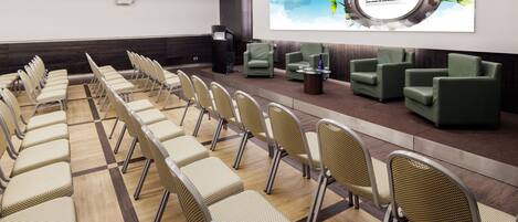 A conference room with rows of chairs, a stage with a podium, and a large screen displaying 'Creative Business' and 'Digital Communication'.