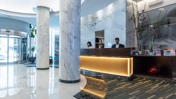 Una hall moderna con colonne in marmo, una reception e un grande vaso di fiori.
