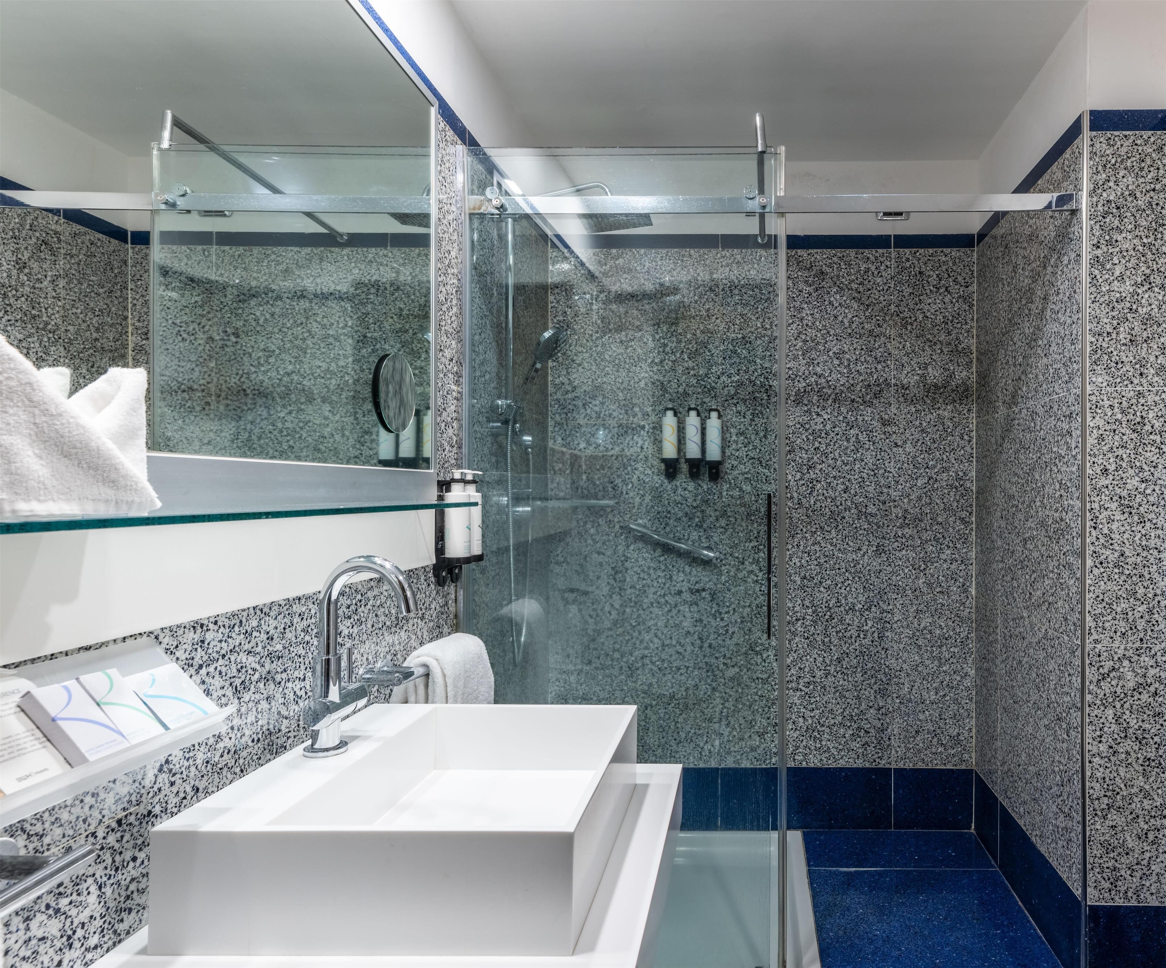 A modern bathroom with a glass-enclosed shower, a white sink, and a mirror above it.