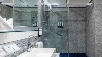 Un bagno moderno con doccia vetro, lavabo bianco e specchio soprastante.
