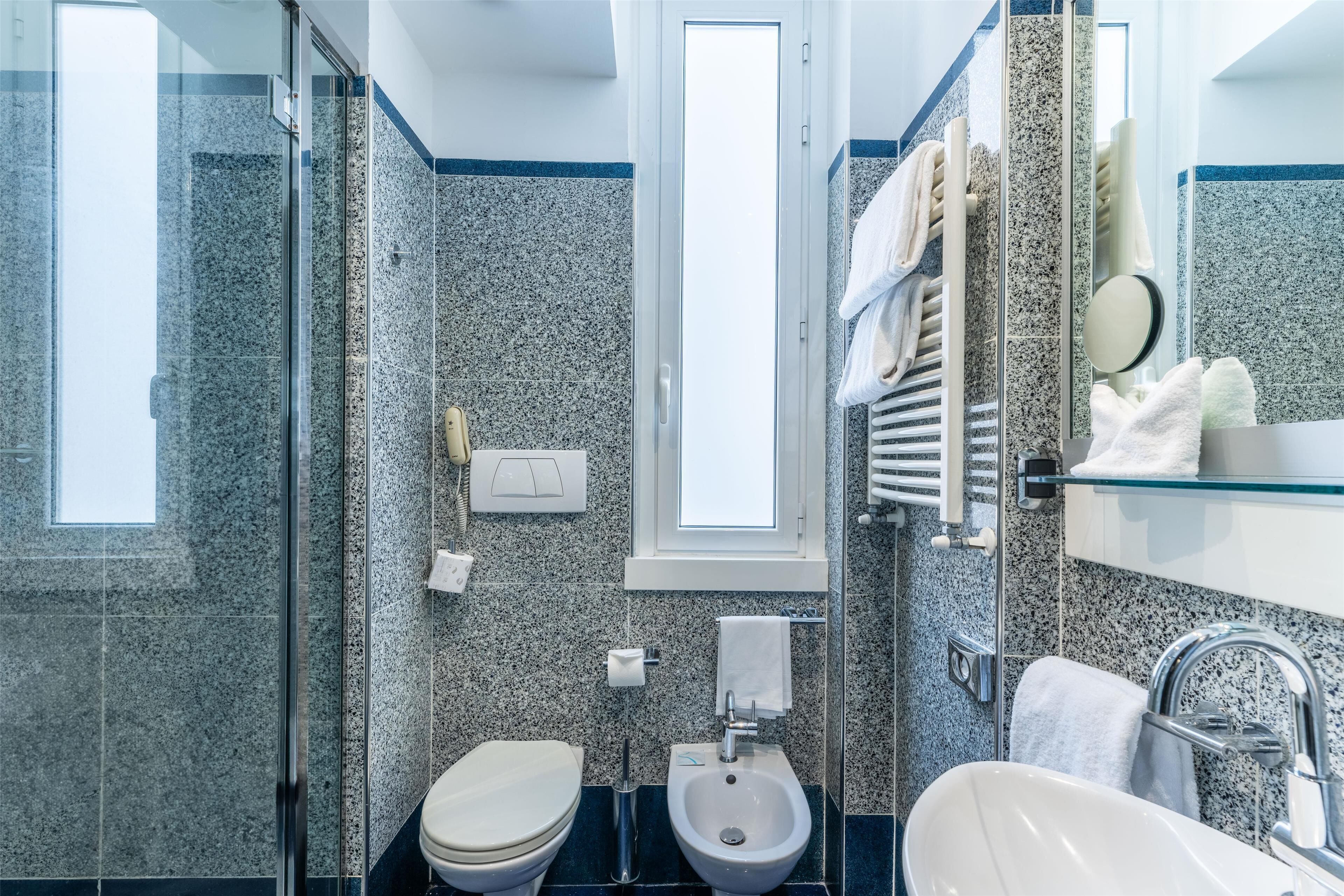 Un baño moderno con cabina de ducha de vidrio, un bidé, un inodoro y un lavabo con espejo.