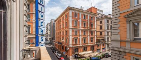 Um hotel com uma placa que diz "UNIVERSO" na fachada, carros estacionados em frente e céu claro.