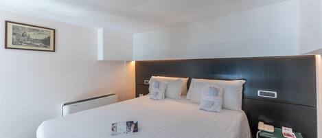 A hotel room with a large bed, white linens, a bedside phone, and a framed picture on the wall.