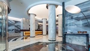 Un hall d’entrée moderne avec des colonnes en marbre, un comptoir d’accueil et une cloison en verre.