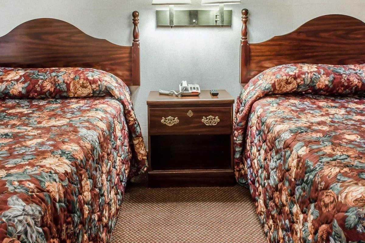 Een hotelkamer met twee bedden, elk voorzien van bloemenbeddengoed, een nachtkastje met een lamp en een telefoon.