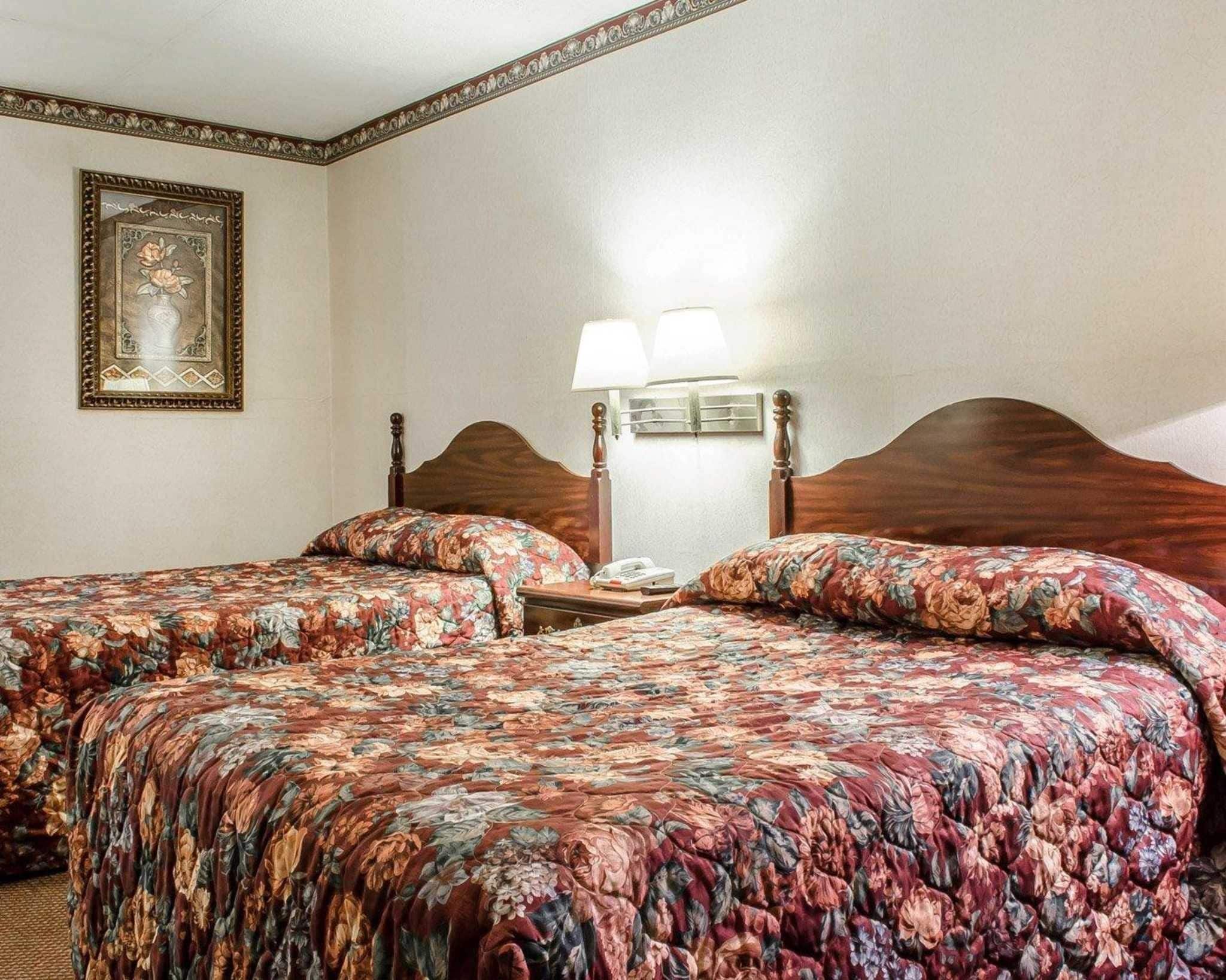 A hotel room with two beds, each with floral-patterned bedding, a nightstand with a lamp, and a framed artwork on the wall.