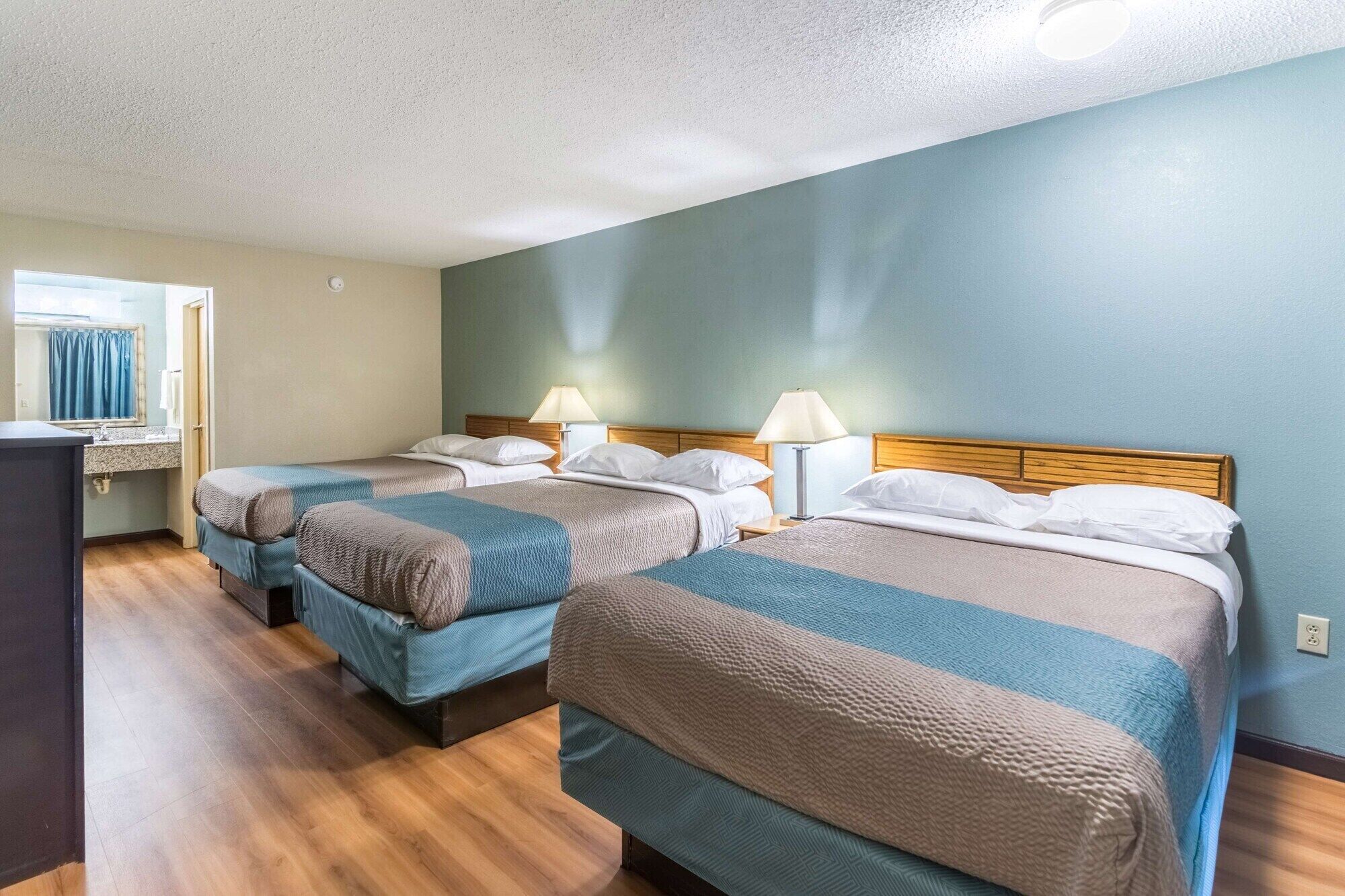 Una habitación de hotel con dos camas, un baño con lavamanos y un ventanal con cortinas.