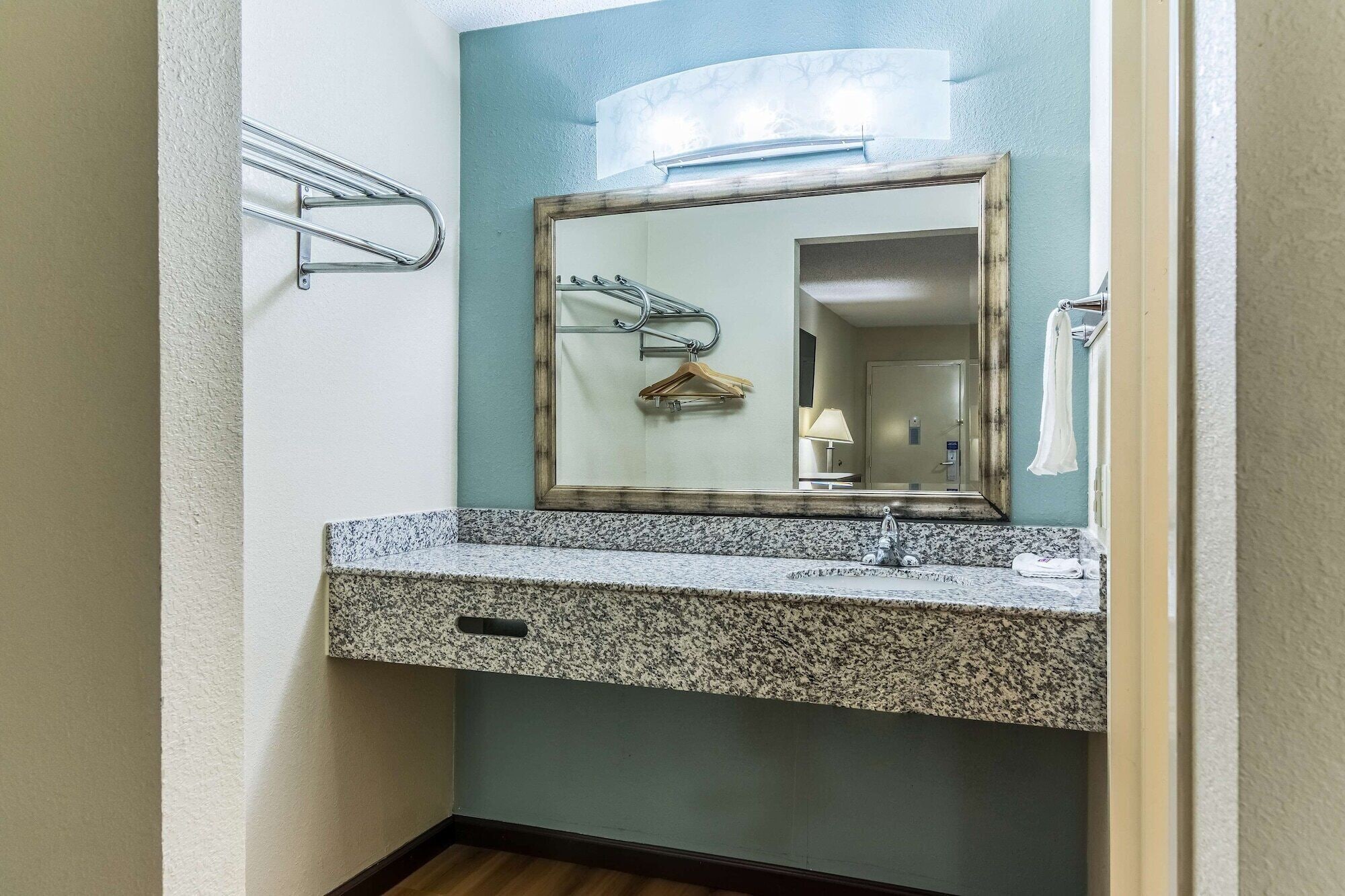 Un baño con encimera de granito, lavabo, espejo y ganchos para toallas.