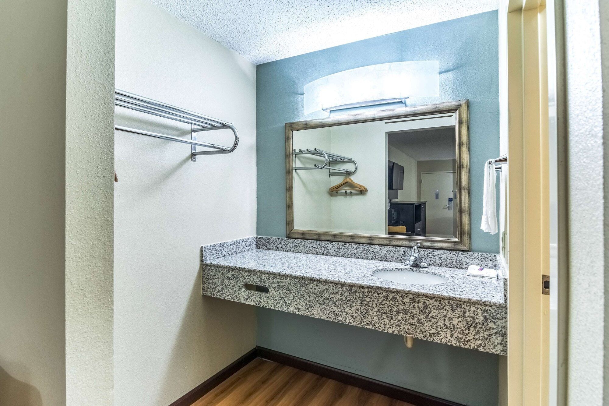 A bathroom with a granite countertop sink, a mirror with a wooden hanger, and a towel rack.