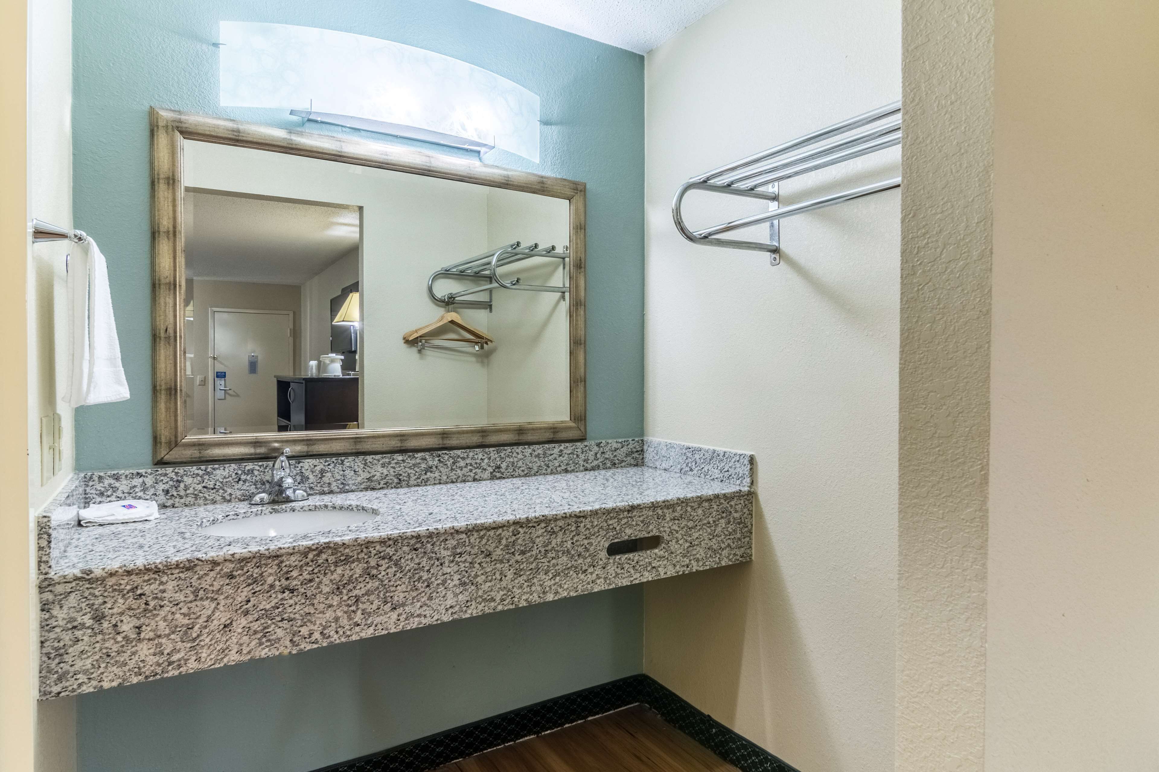 A bathroom with a granite countertop sink, a mirror with a wooden frame, and a towel rack.