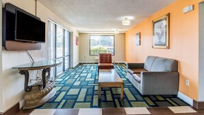 A hotel lobby with a large TV, a patterned carpet, a sofa, a chair, and a table. - Motel 6 Kenly, NC (Kenly)