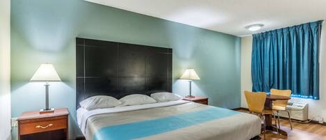 Une chambre d’hôtel comprenant un lit, deux tables de chevet avec des lampes, un bureau avec une chaise et une fenêtre avec des rideaux.
