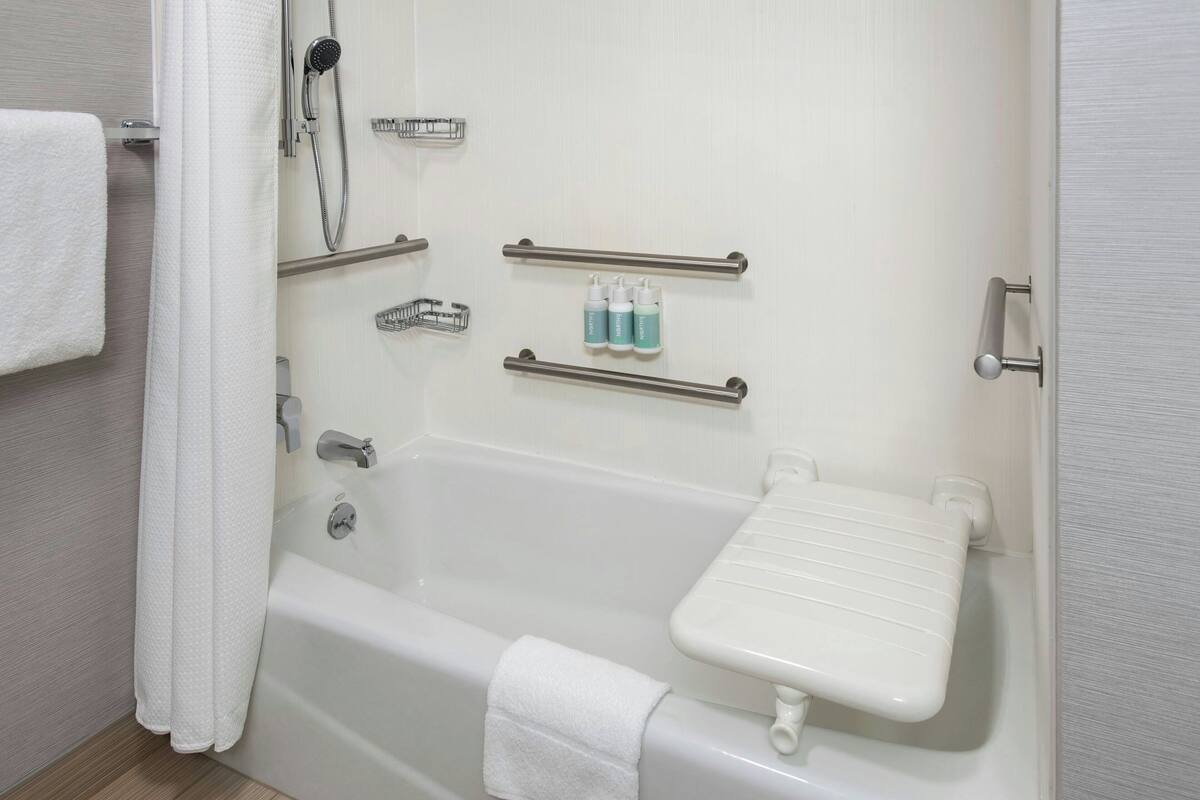 A bathroom with a bathtub, a showerhead, a towel rack, and a shelf with toiletries.