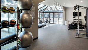 A gym with exercise equipment, a wall-mounted TV, and a large window providing natural light. - Courtyard by Marriott Rye (Rye Brook)
