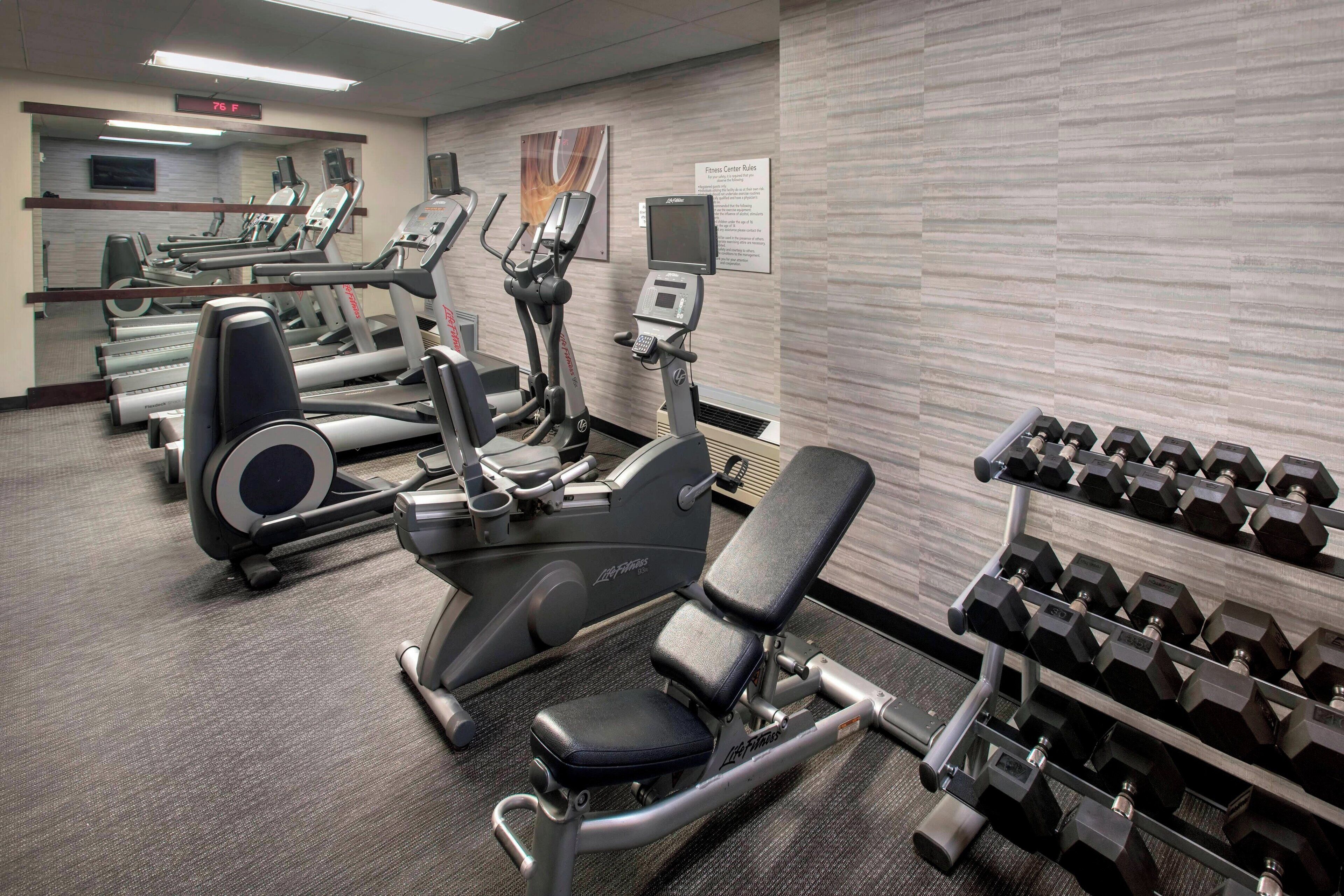 A gym with treadmills, elliptical machines, a bench press, and a rack of dumbbells.