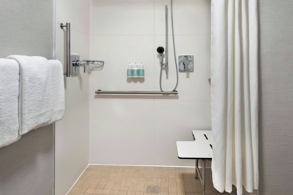 A modern bathroom with a shower, a towel rack, a small table, and toiletries on the wall.