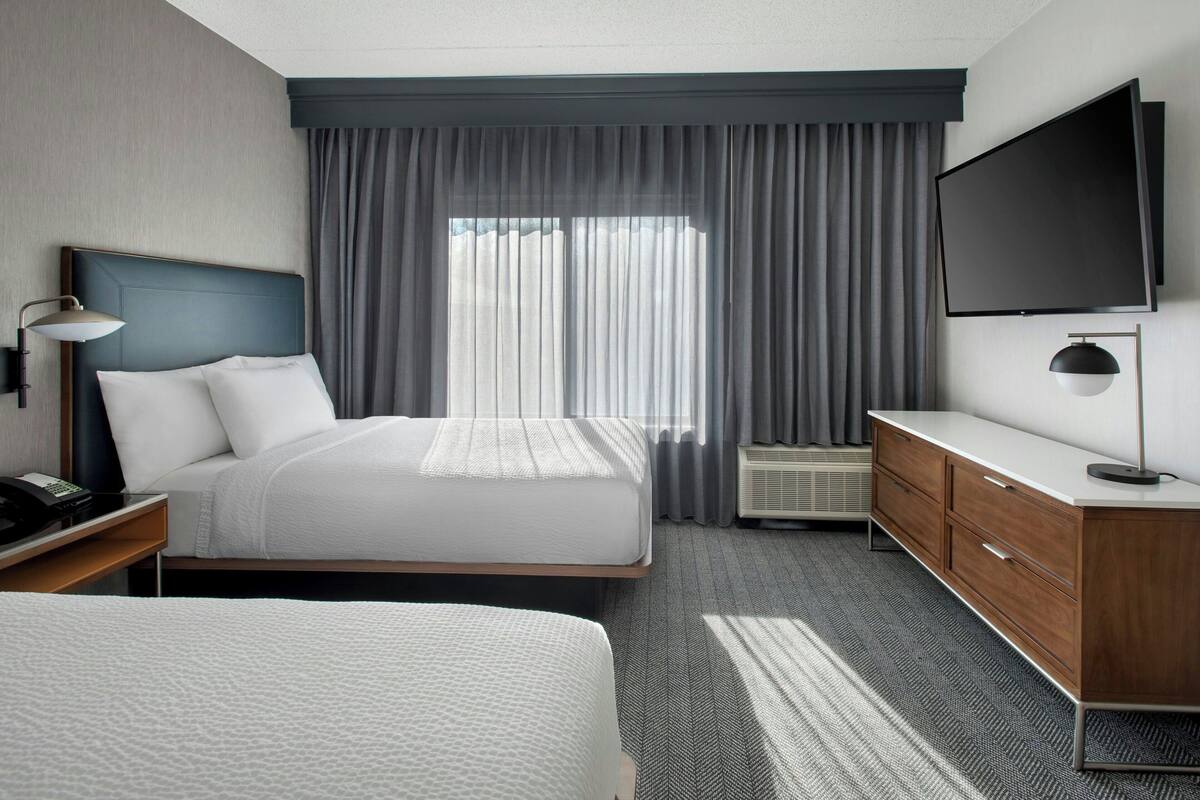 A hotel room with a large bed, a TV, a desk with a lamp, and a dresser.