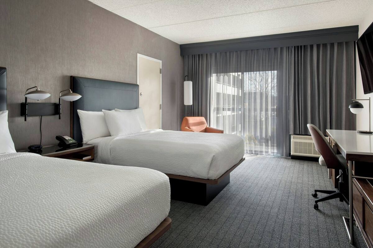 A hotel room with two beds, a desk, a chair, a telephone, and a window with curtains.
