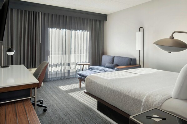 A hotel room with a bed, a desk, a chair, a lamp, and a window with curtains. - Courtyard by Marriott Rye (Rye Brook)