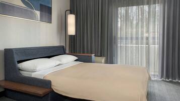 A modern hotel room with a bed, a bedside table, a lamp, and a large window with curtains.